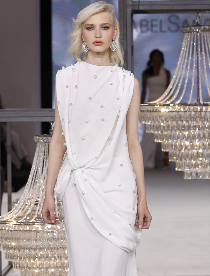 Una modelo camina por la pasarela luciendo un vestido blanco elegante.