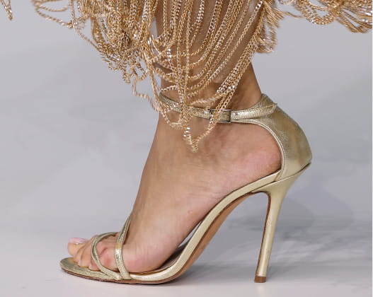 Primer plano de sandalias doradas metálicas en los pies de una mujer, resaltando su brillo y atractivo visual.