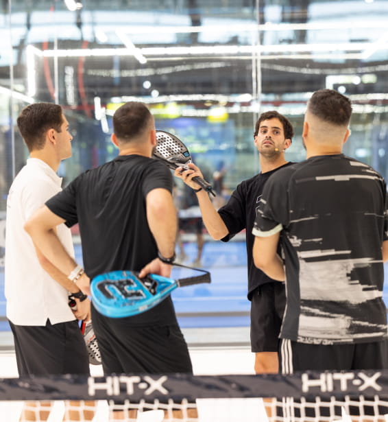 Cuatro hombres de pie frente a una red, participando en una actividad de padel.