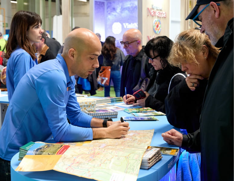 Hombre expositor indicando en un mapa mientras ofrece información a los visitantes en el salón de B-Travel.