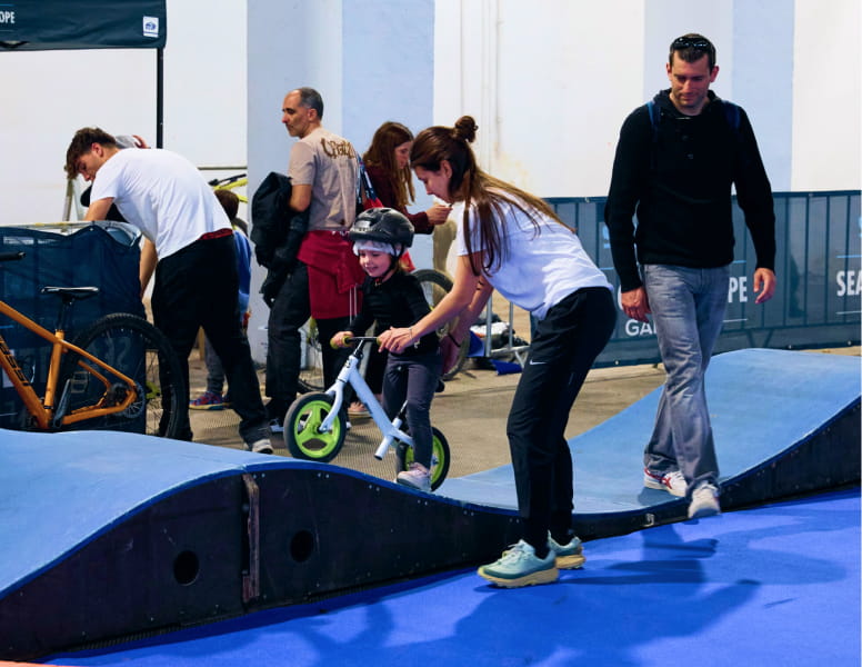 Monitora ayundado a un niño pequeño a montar en bici por una rampa